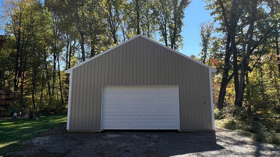 A garage with a white garage door is sitting in the middle of a forest.