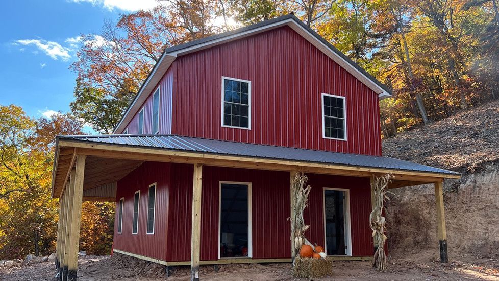 A large red barn with a porch is sitting on top of a hill.