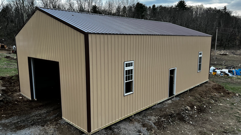 A large metal building with a brown roof is sitting in the middle of a dirt field.