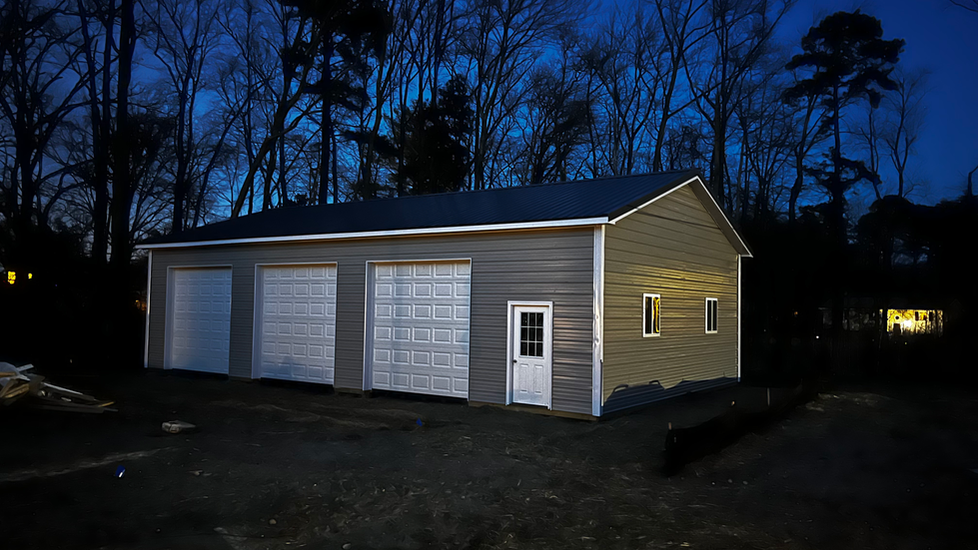 A garage with two garage doors is lit up at night.
