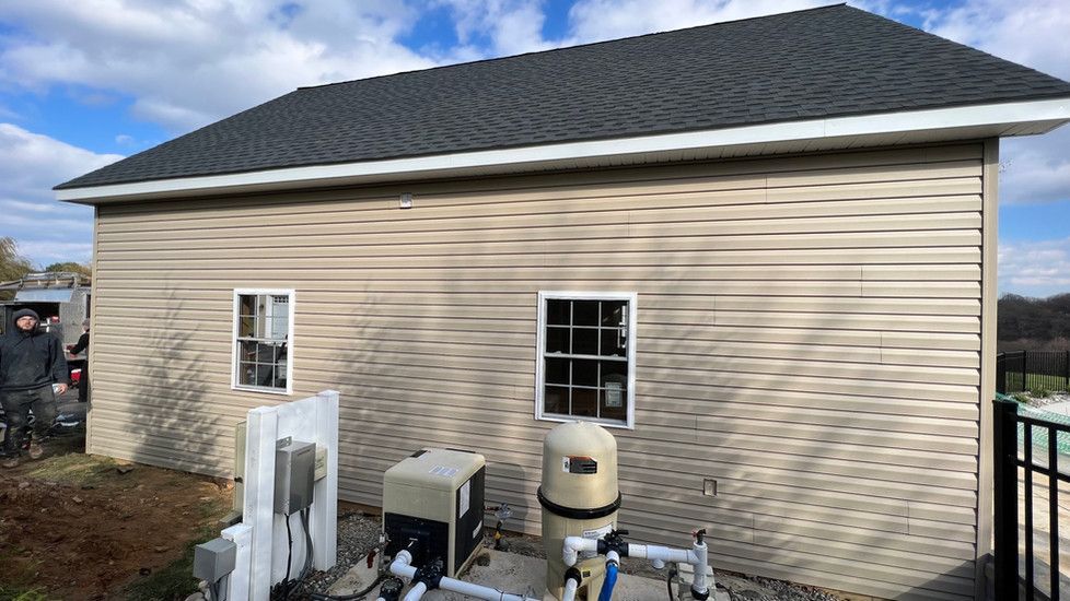 A house with a black roof and a pool pump on the side of it.