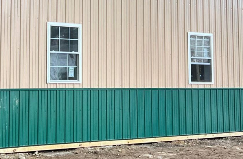 The side of a building with green siding and two windows.