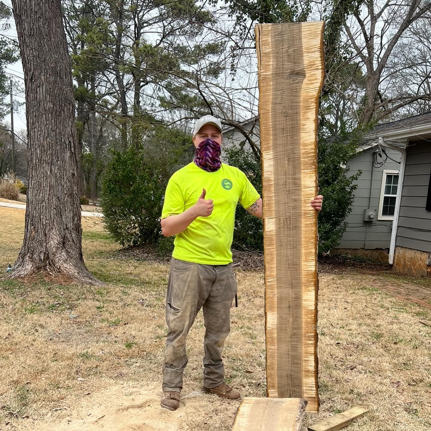 A man is standing next to a large piece of wood and giving a thumbs up.