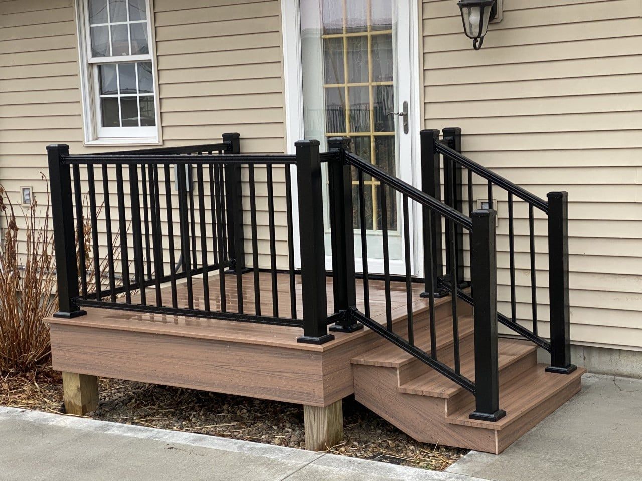 A composite deck with black railings and stairs leading to a white door, against beige siding.