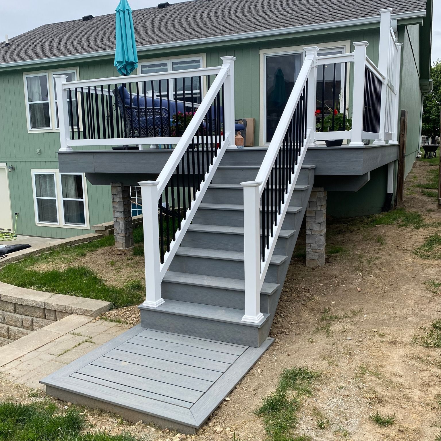 Gray deck with stairs, white and black railings, and a ramp leading to the ground.