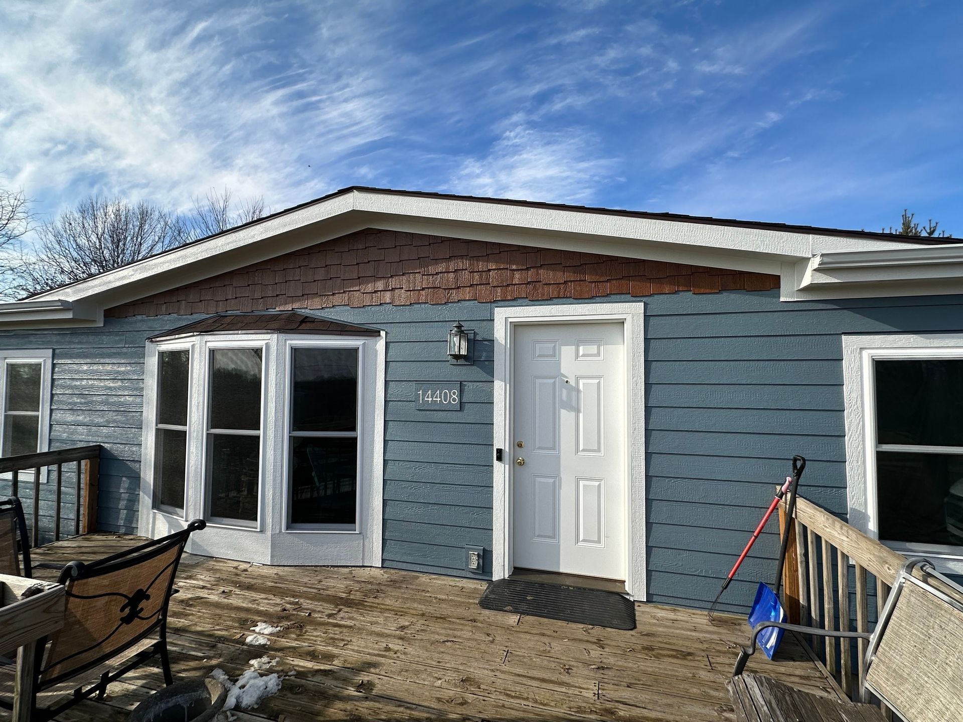 Blue house with white trim and door, brown roof and porch, and a bright blue sky.