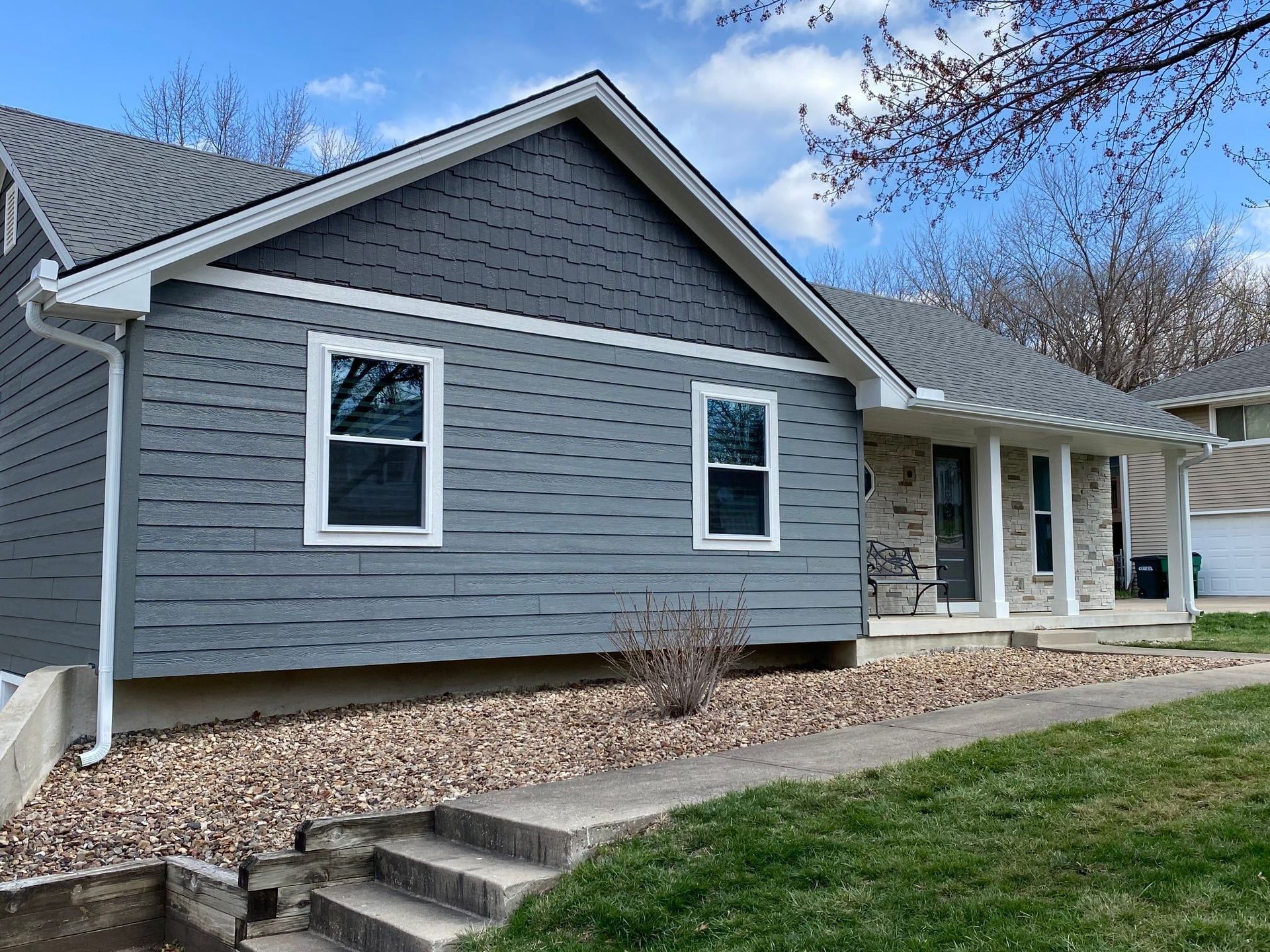Gray house with gray siding and white trim, rock landscaping, and a concrete walkway.