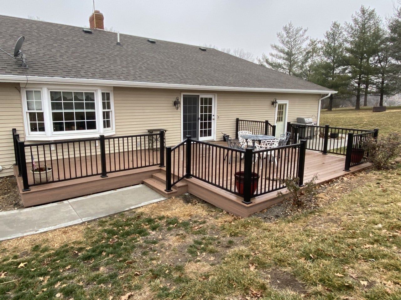 A backyard deck with black railings and brown wood, attached to a beige house with a sliding door.