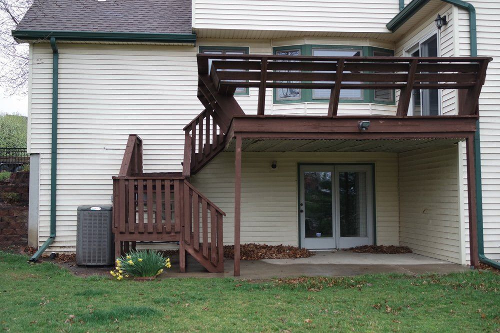 A two-story house with a brown deck and stairs, AC unit, and a door leading outside.