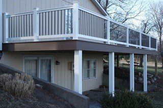 Beige house with deck supported by white columns; brown decking and white railing.