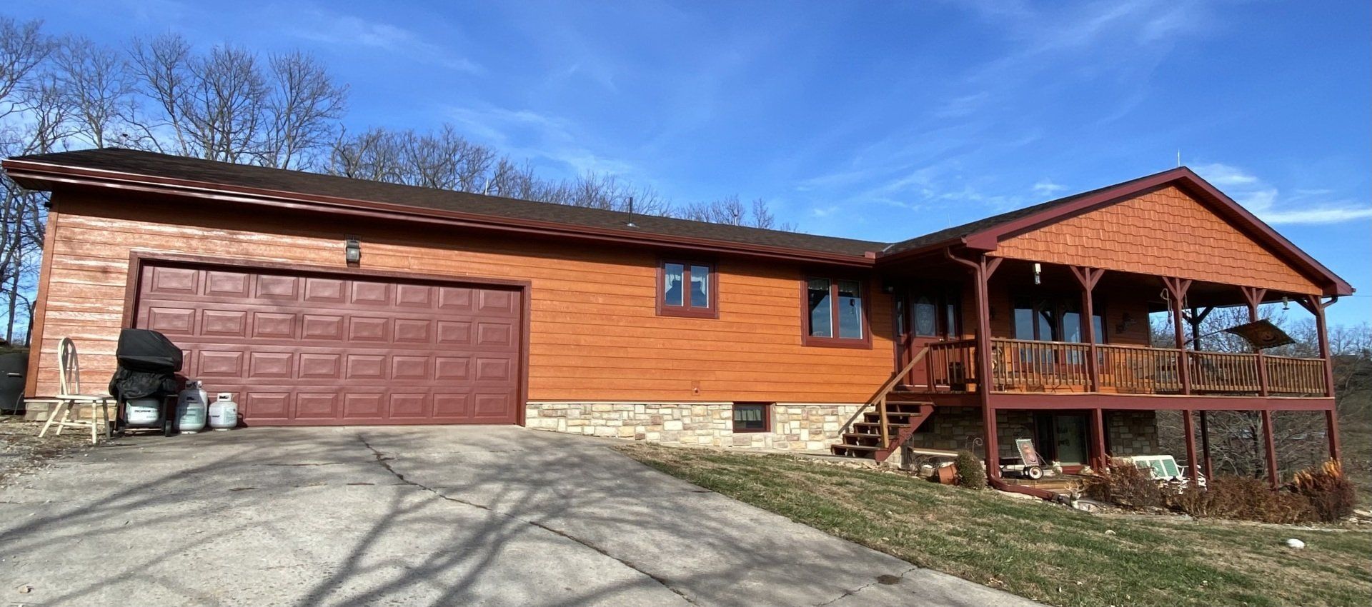 Wooden house with a garage and porch under a blue sky.