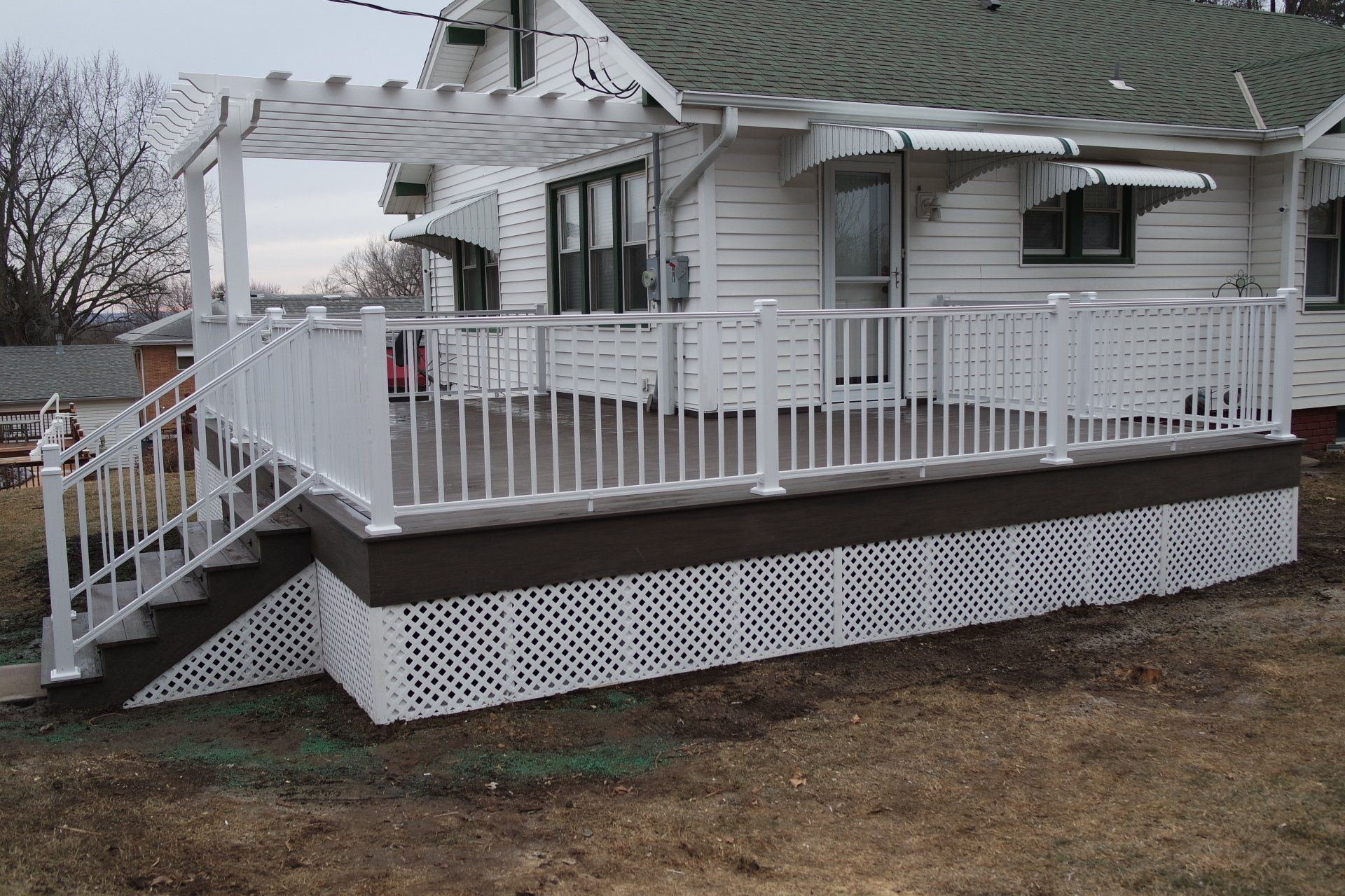 White deck with pergola, latticework, and steps in front of a white house.
