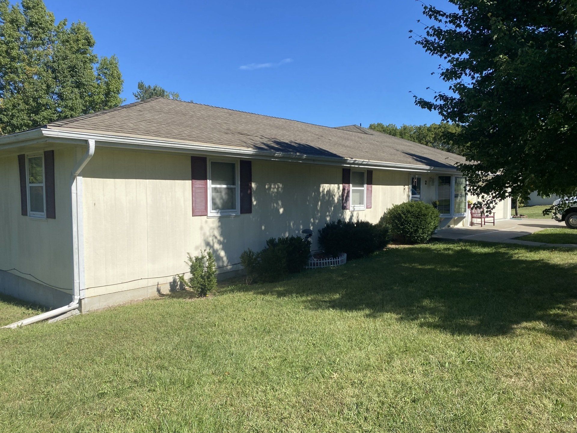 A tan, single-story building with a gray roof and burgundy shutters sits on a green lawn under a blue sky.
