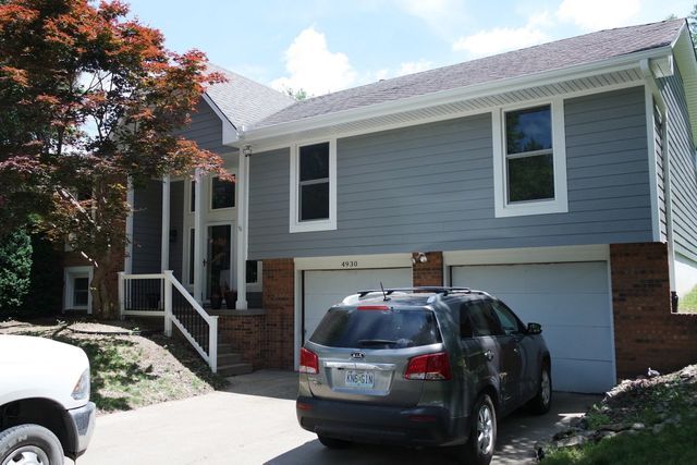 Two-story gray house with white trim, two-car garage, and a vehicle parked in the driveway.