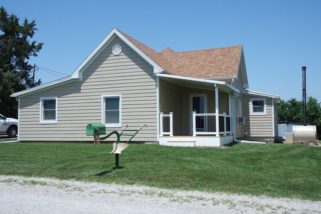 Tan house with brown roof, green lawn, white porch and mailbox. Bright sunny day.