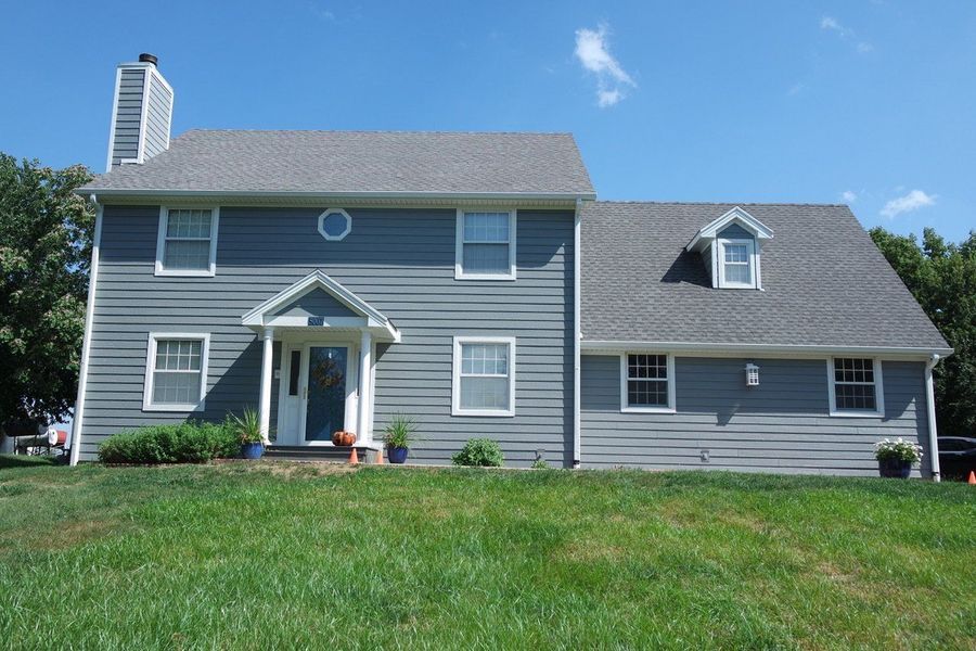 Blue-gray two-story house with a grassy lawn under a blue sky.