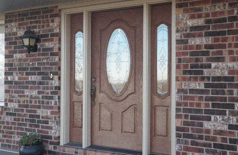 Brown wooden front door with sidelights, set in a brick wall; exterior of a house.