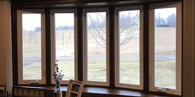 Five-paneled bay window, partially open, overlooks a field and trees.