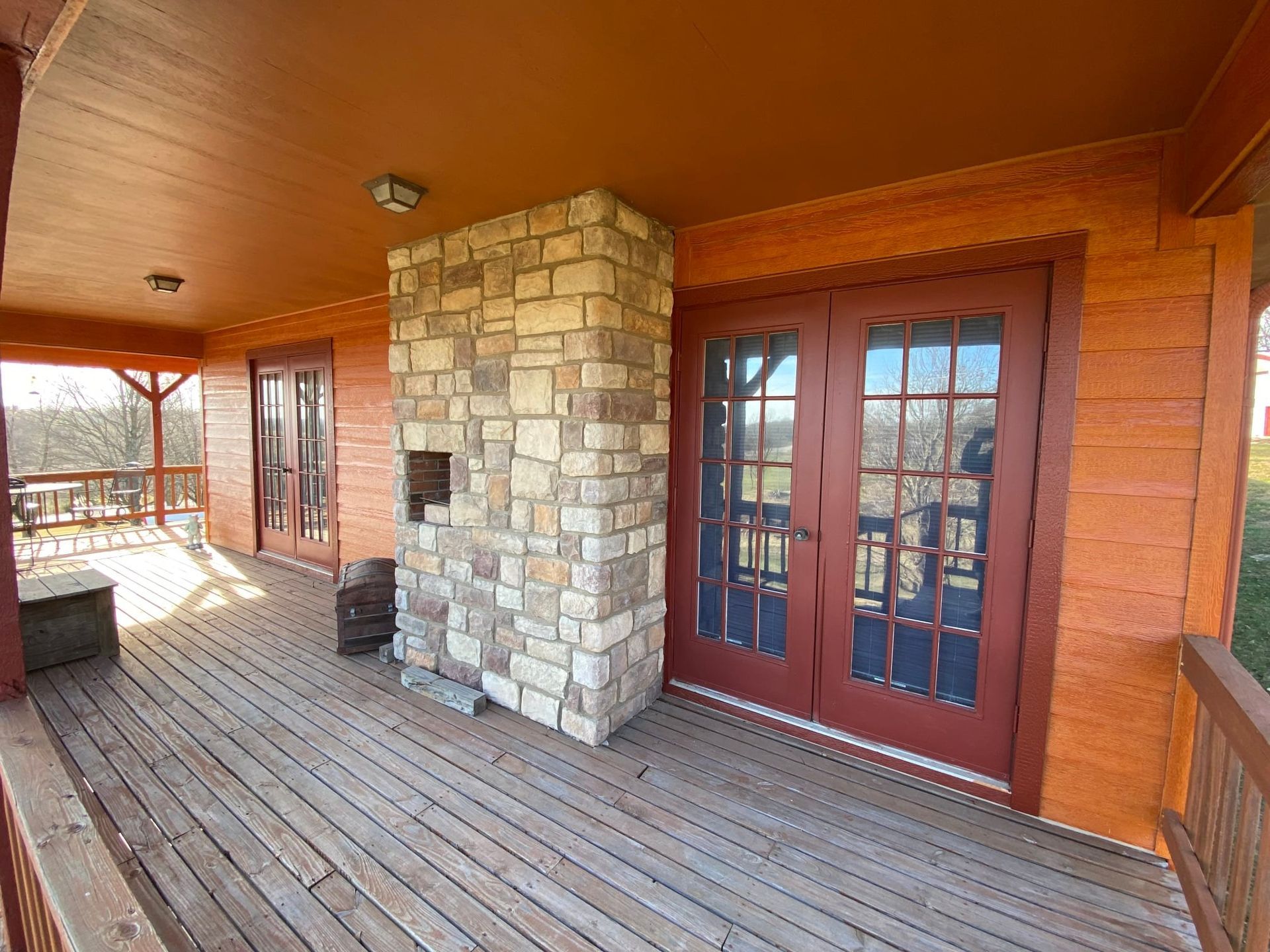 Wood porch with stone chimney and red doors, overlooking a wooded area.