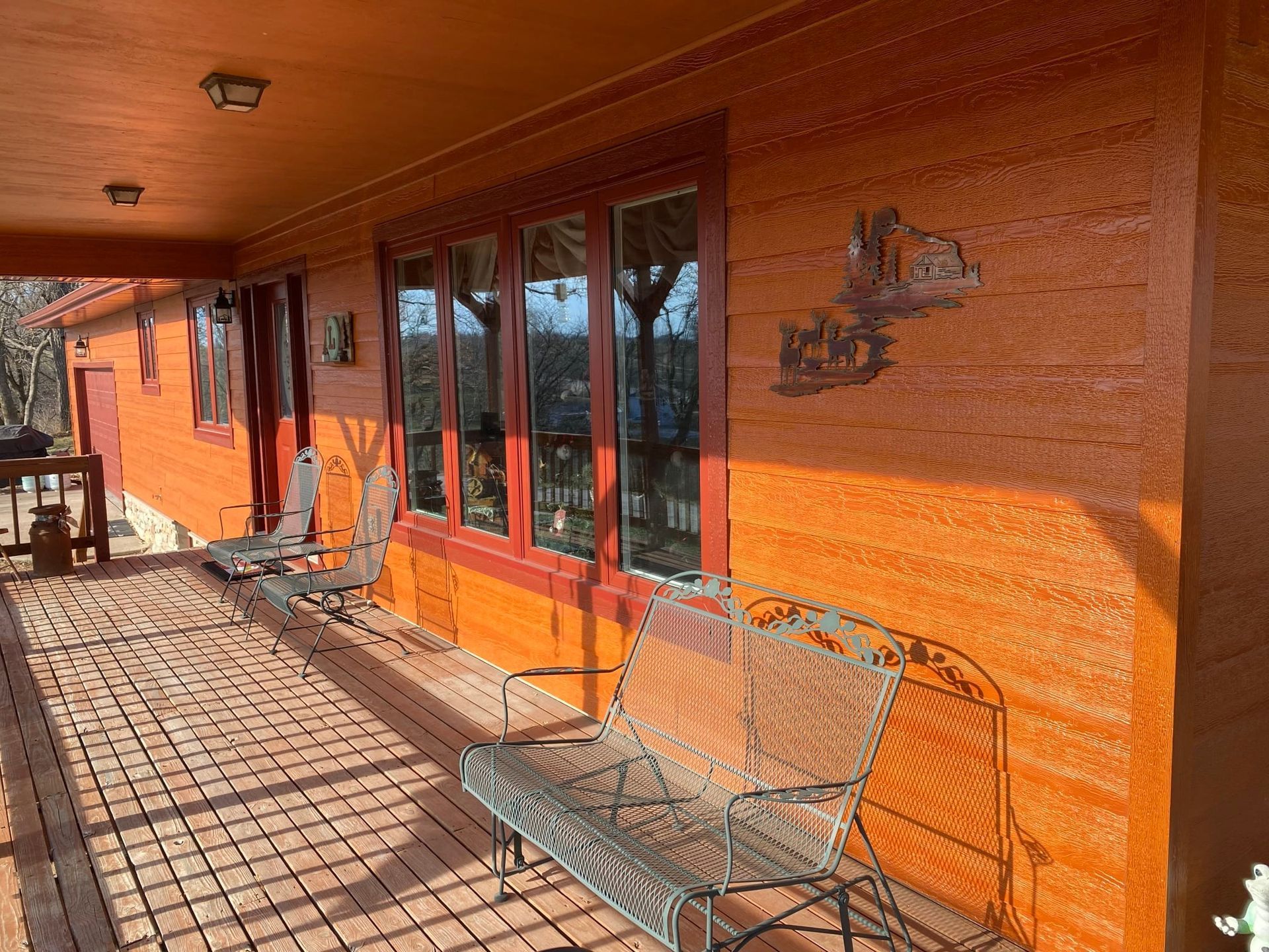 Orange-colored adobe house with porch, brick floor, metal bench, and windows; sunny outdoor setting.