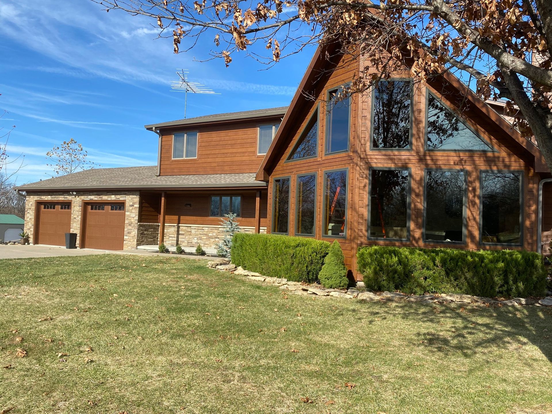 Brown wooden house with large windows and a two-car garage on a green lawn.