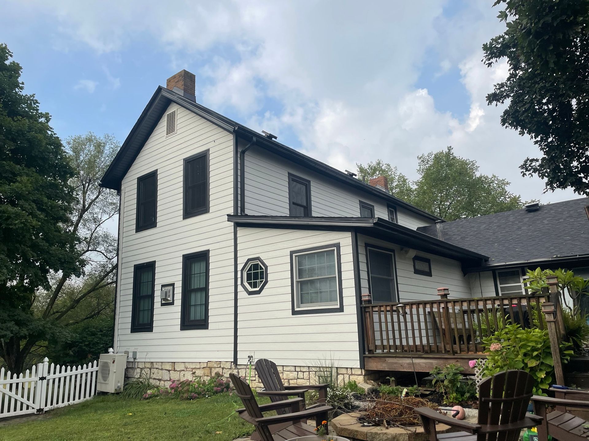 Two-story white house with black trim, deck, and white picket fence under a cloudy sky.