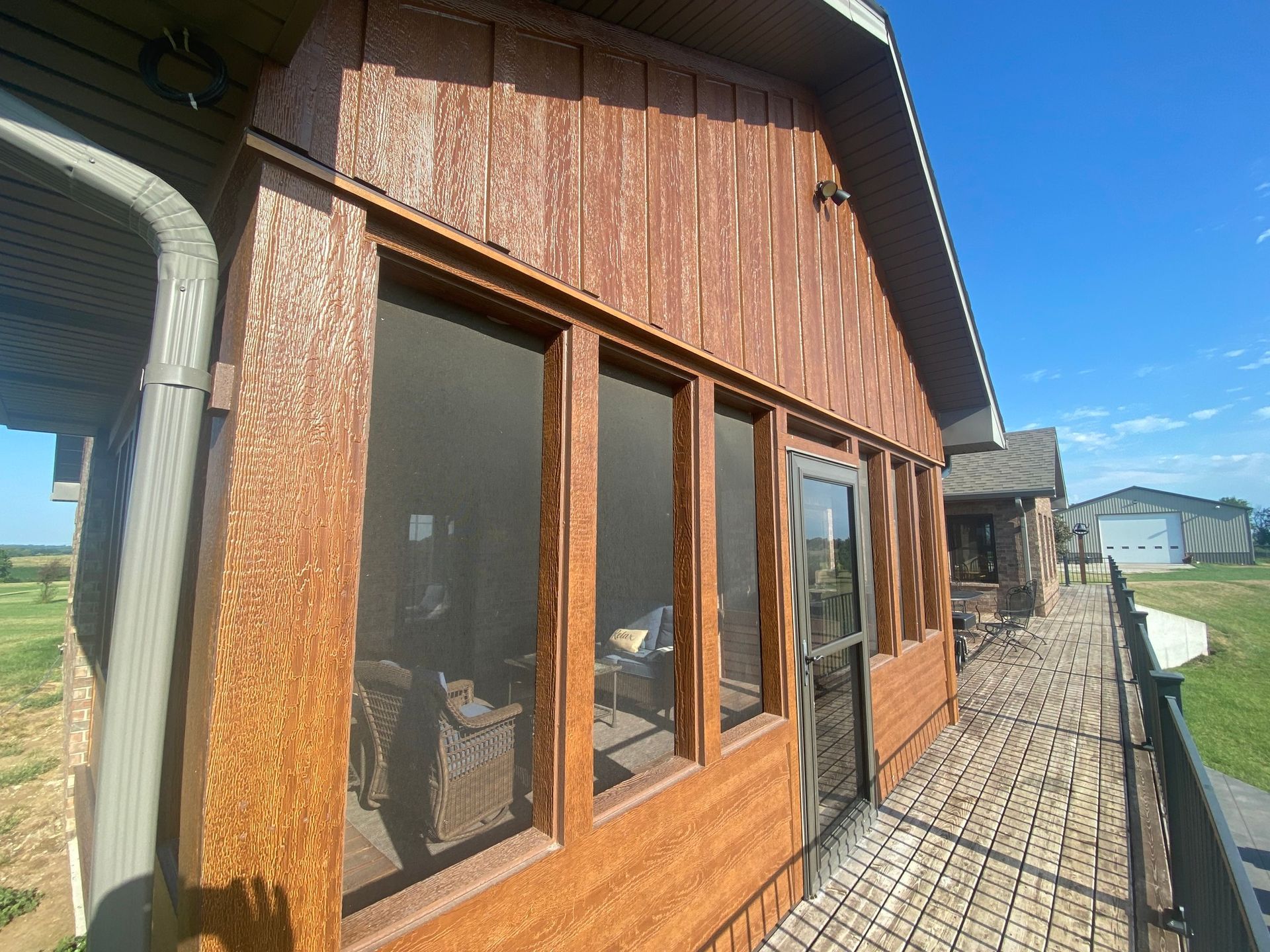 Exterior view of a wood-paneled sunroom with screened windows, door, and walkway, under a blue sky.