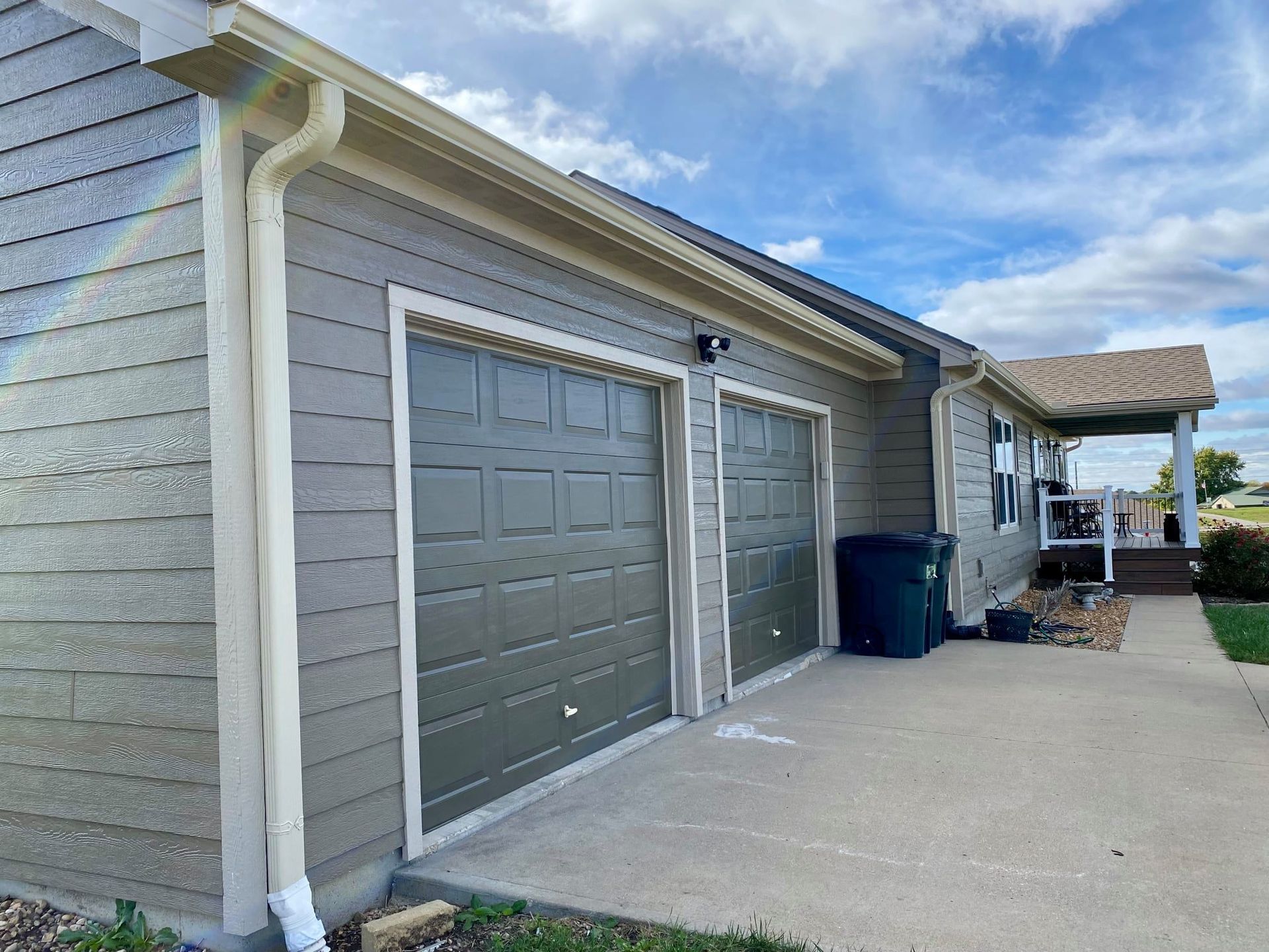 A house with two gray garage doors and a concrete driveway. Beige trim, green siding and a blue sky.