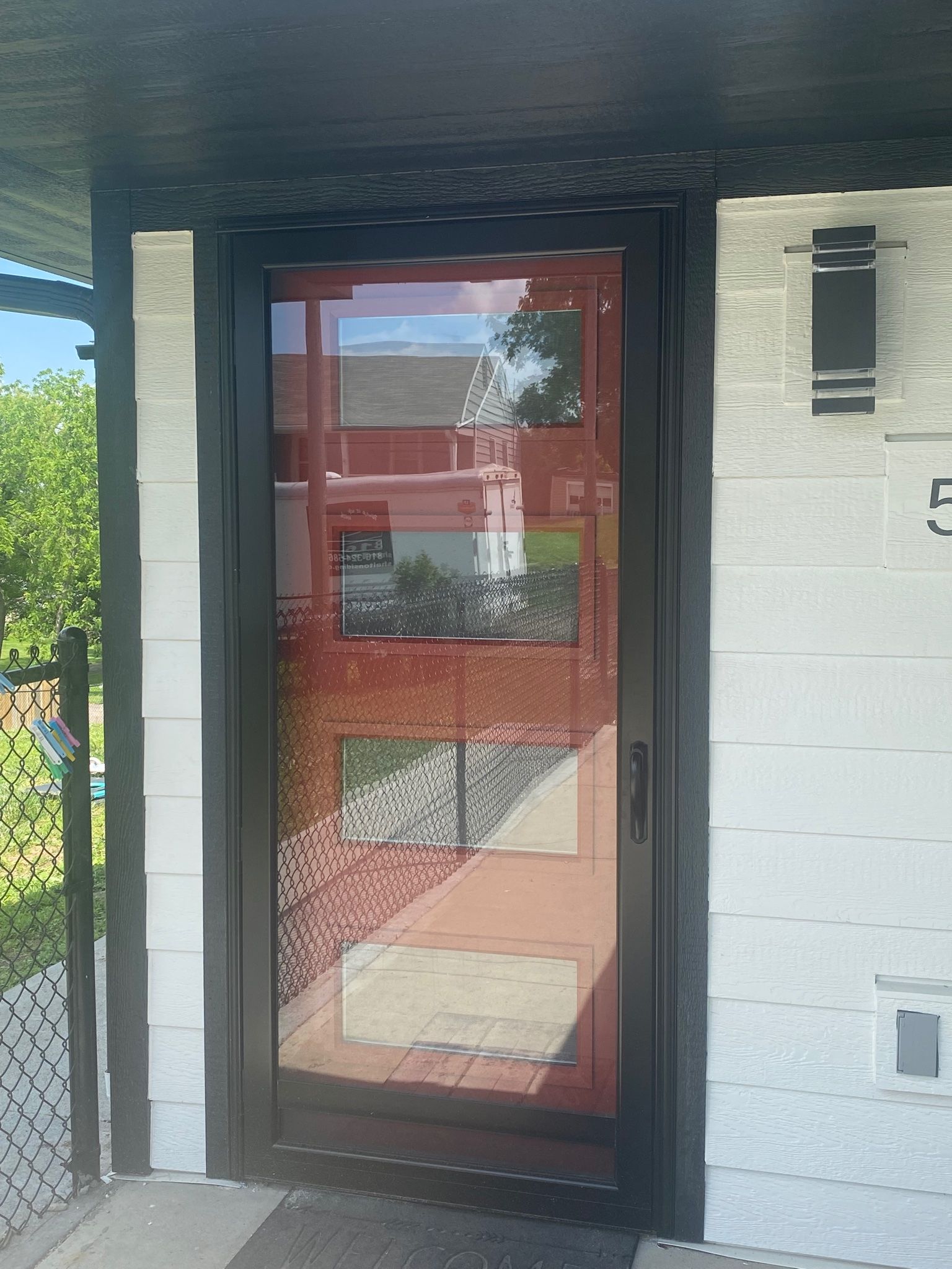 A black-framed front door with textured glass; a white house exterior; a black modern light fixture.