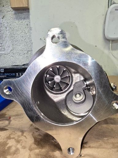 Silver-colored turbocharger with a visible turbine wheel and wastegate.