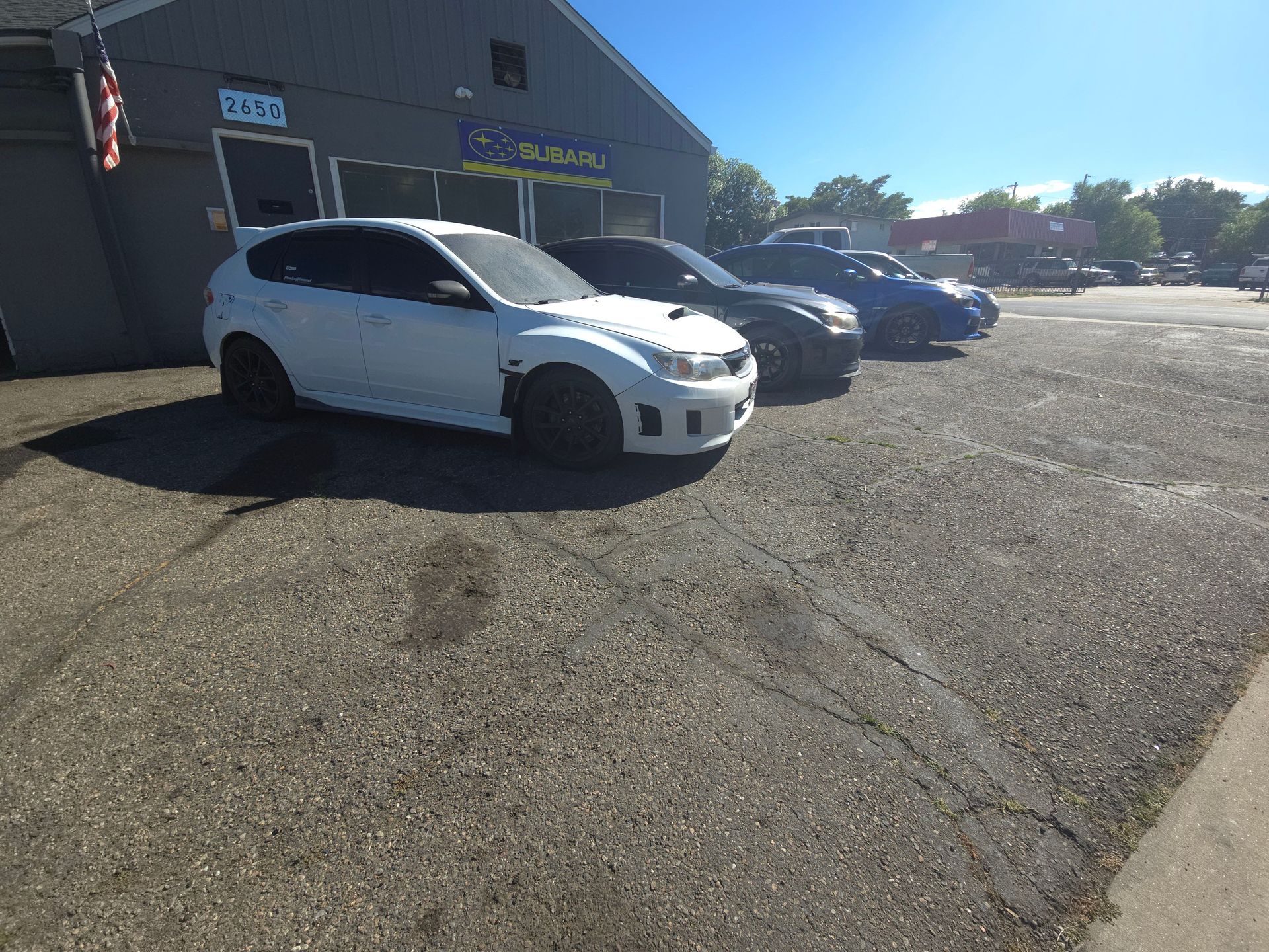 White, black, and blue cars parked in front of a grey building with a blue sky overhead.