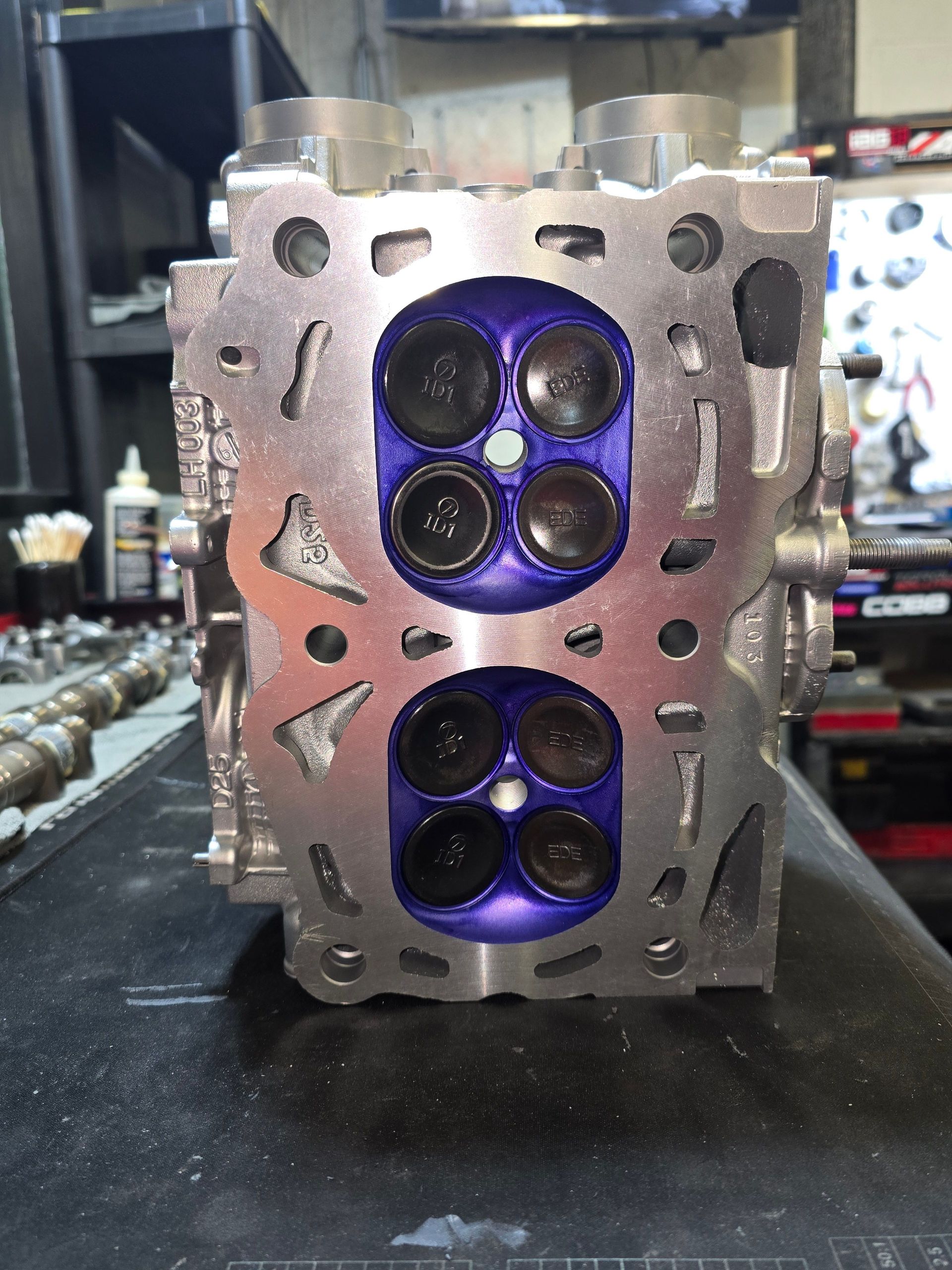 Engine cylinder head with purple detailing, exposed valves, in a workshop setting.