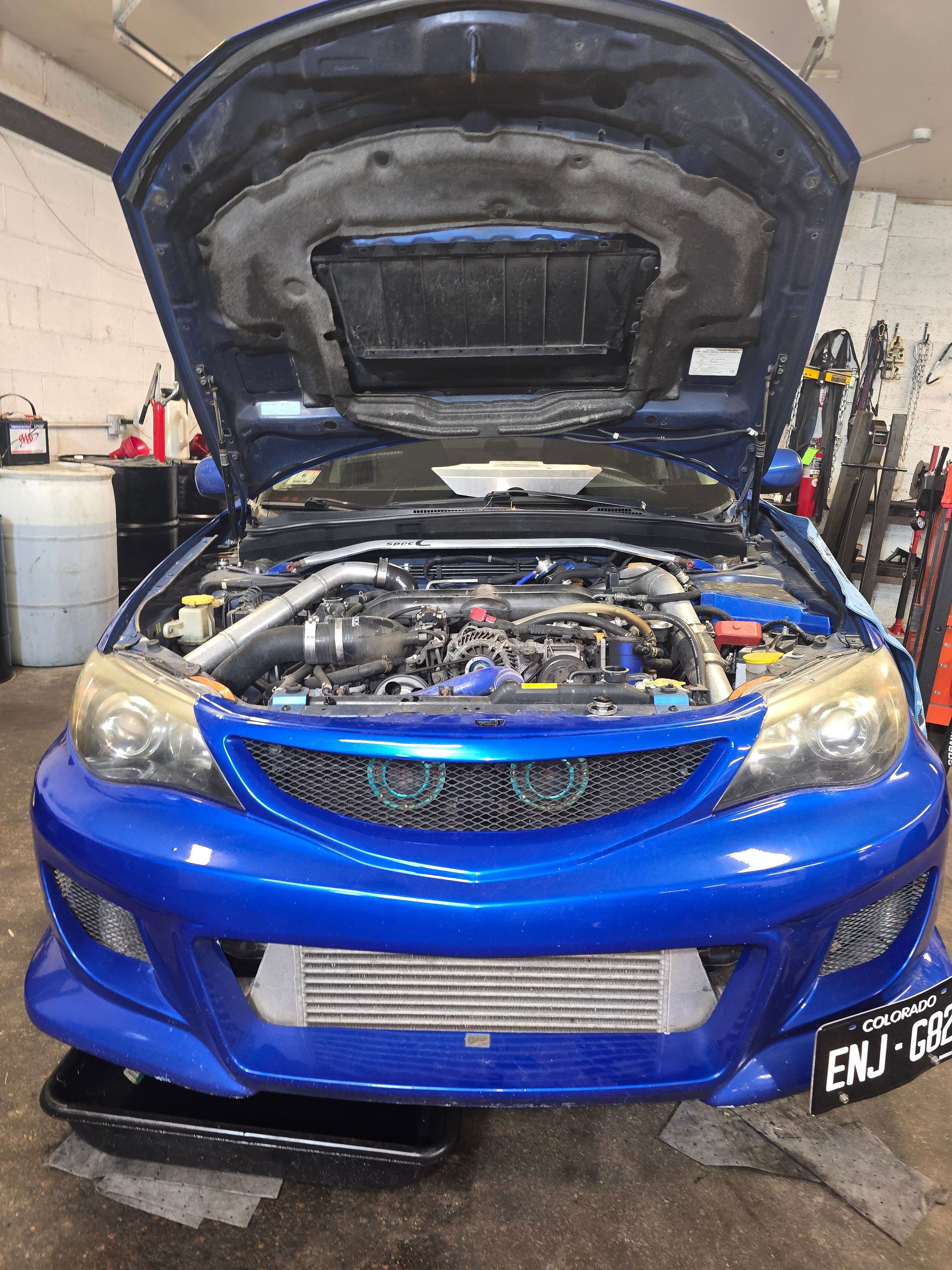 Blue Subaru with hood open, showing engine details in a garage.