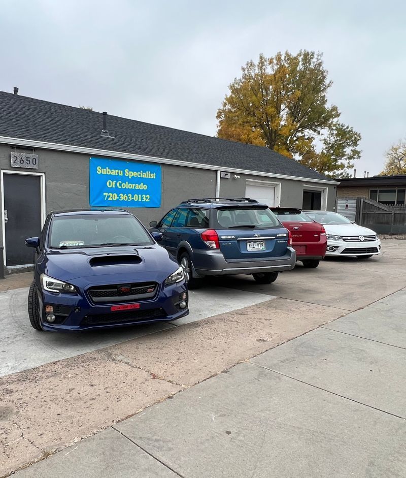 Cars parked outside a blue building with a sign. The building is in a row, with a tree visible in the background.