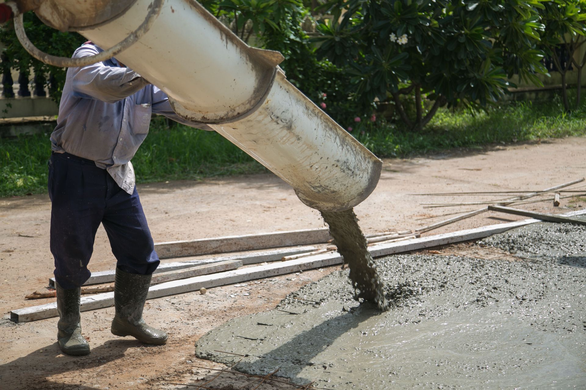Person pouring wet concrete from a chute onto a paved area; outdoor daytime setting.