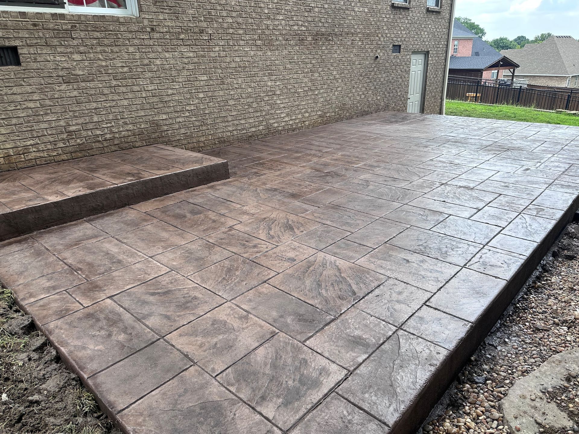 Stone patio beside a brick wall, with a raised step and a wet paved surface.