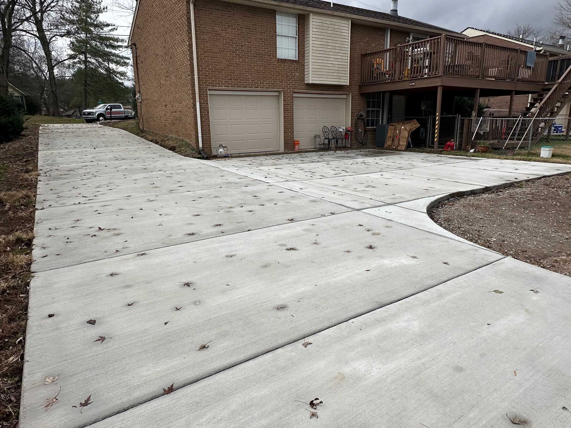 concrete driveway with connected sections leading to a brick building with garage doors and a wooden deck