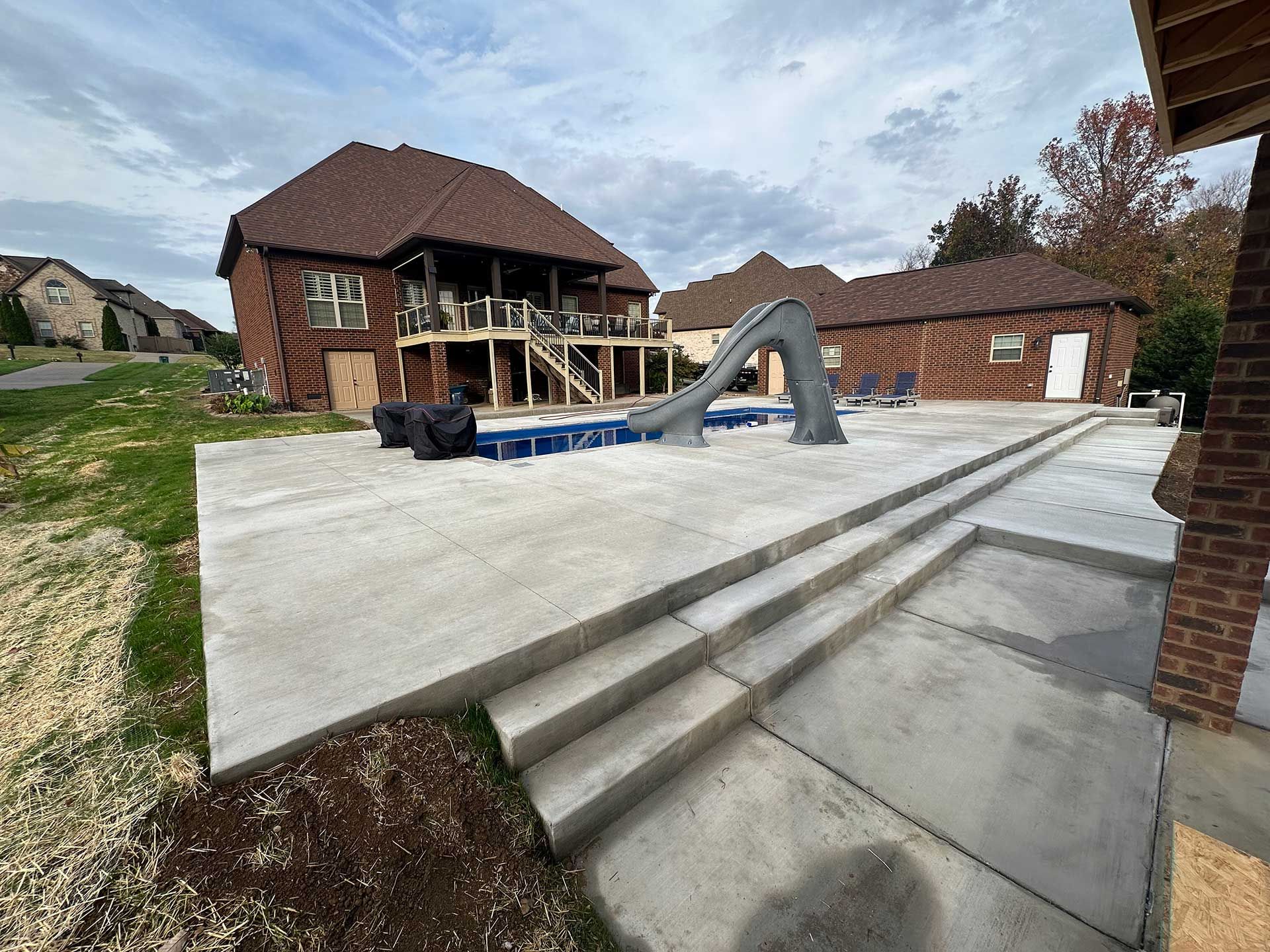 concrete patio with steps leading to pool slide and house with a deck