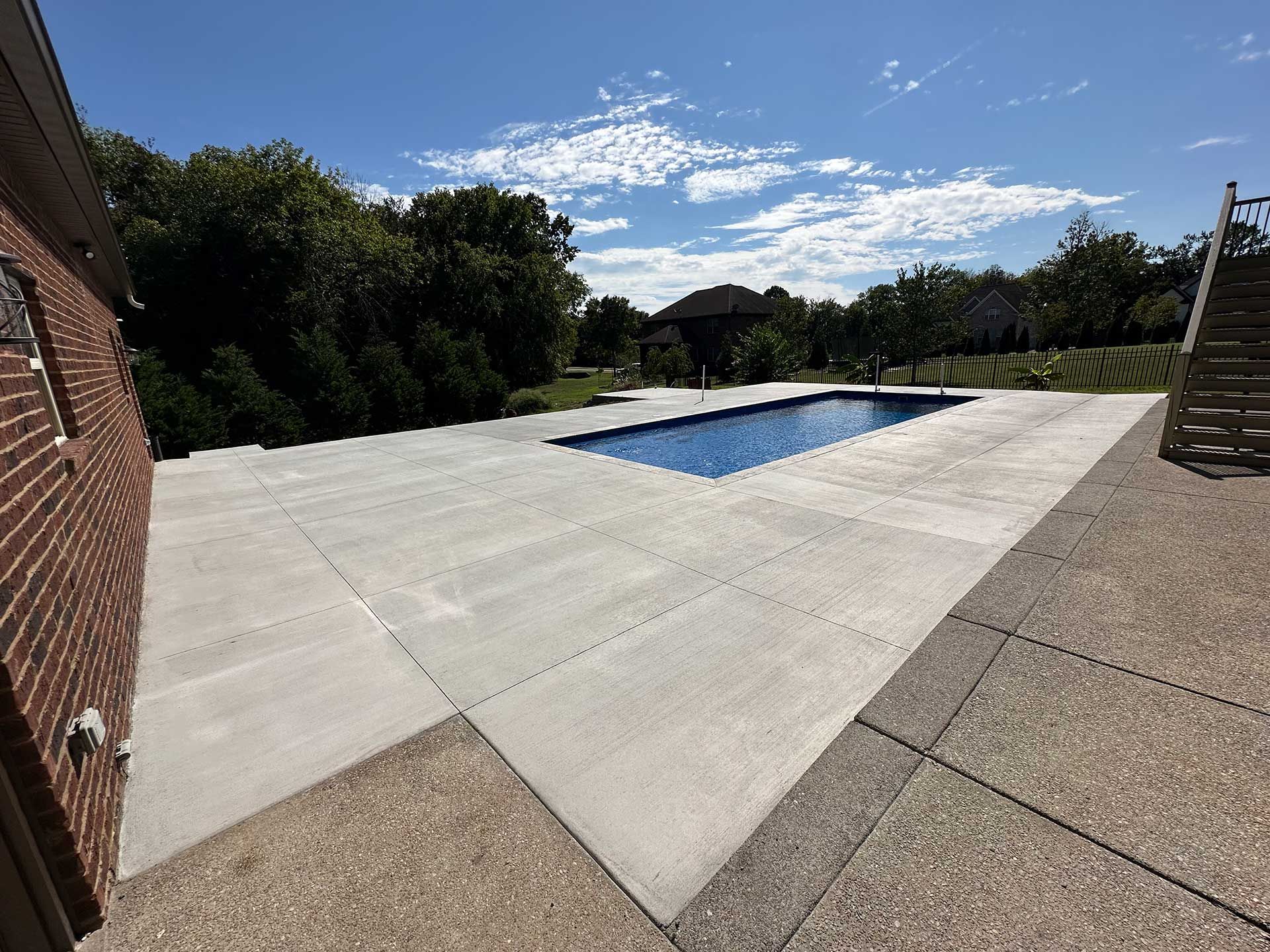 a rectangular swimming pool surrounded by concrete, next to a brick building under a sunny sky