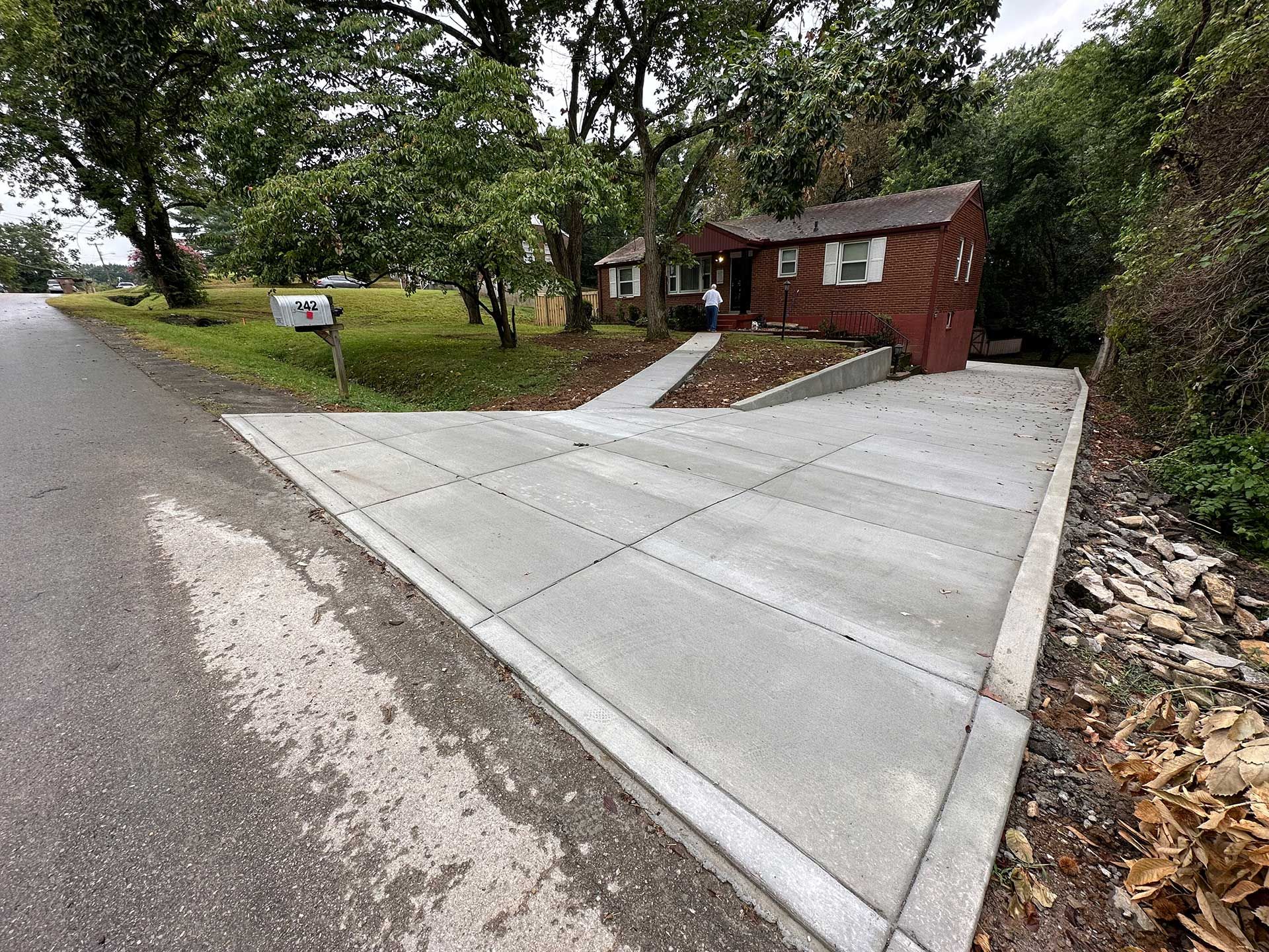 concrete driveway leading to a brown house with a mailbox on a green lawn