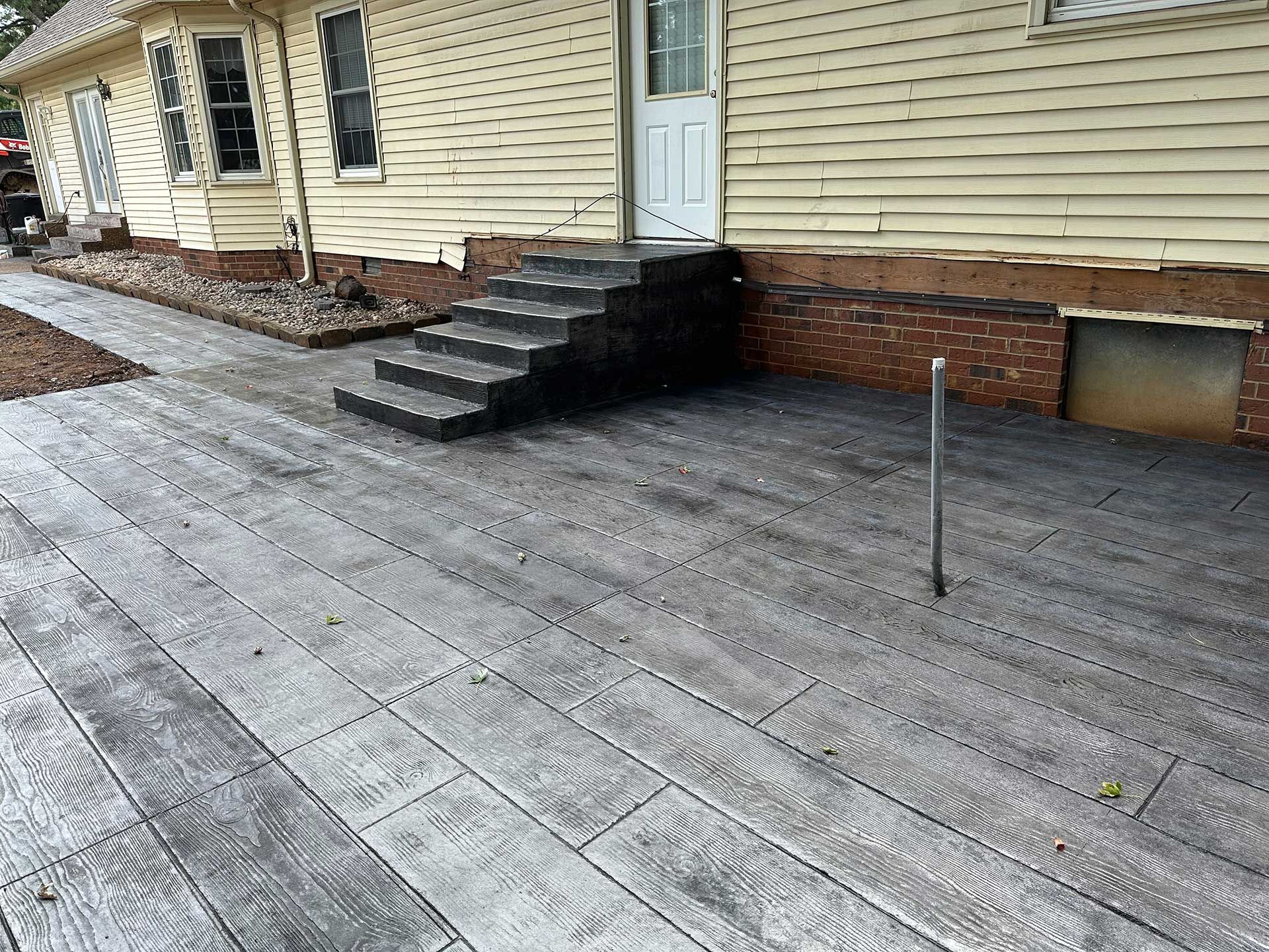 concrete patio with a wood-plank pattern, steps and a door of a light yellow house