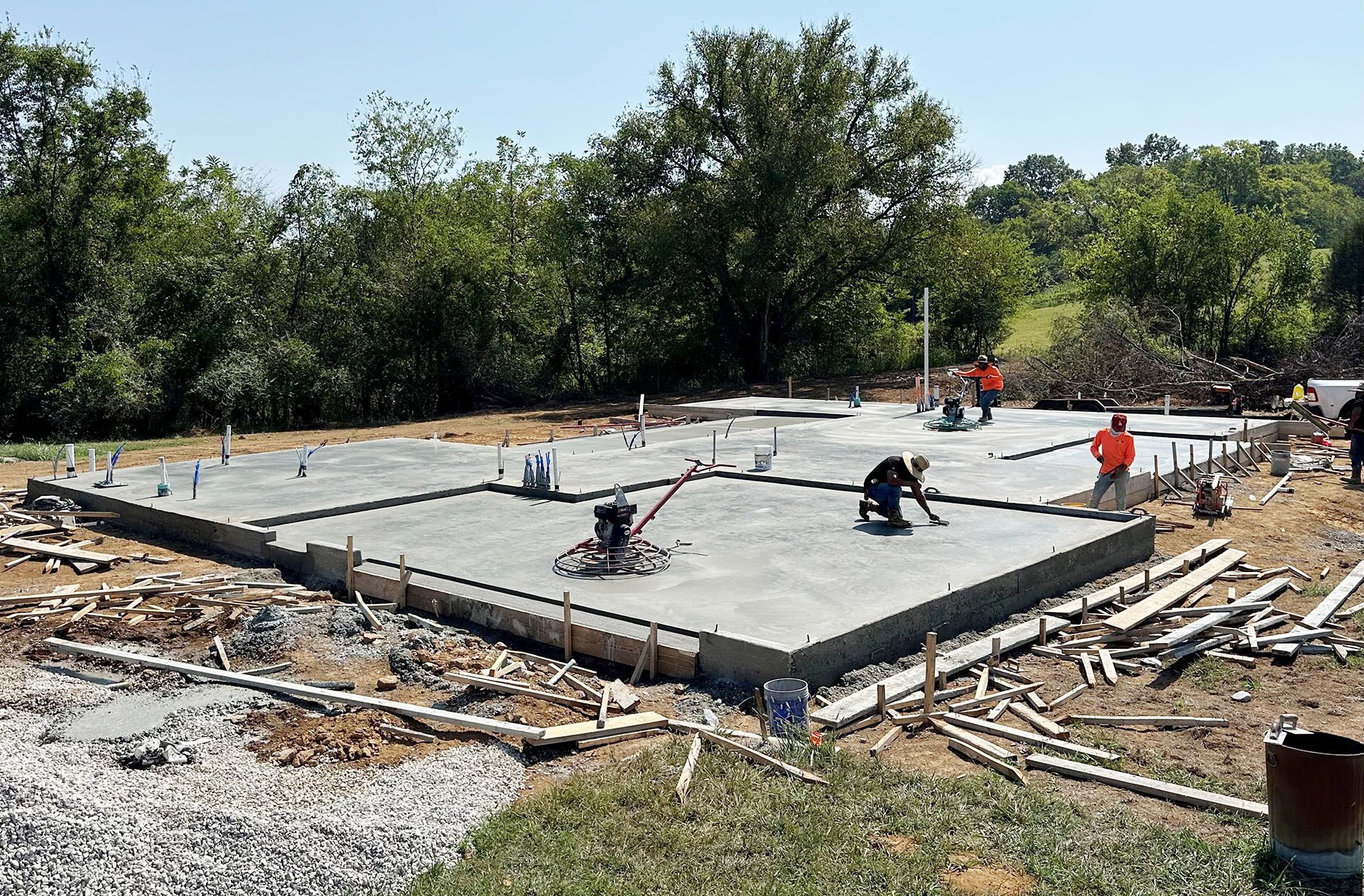 Construction site with a poured concrete foundation. Workers finishing and smoothing the surface.