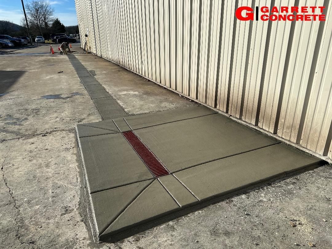 Newly poured concrete sidewalk with drainage. Building in background, Garrett Concrete logo.
