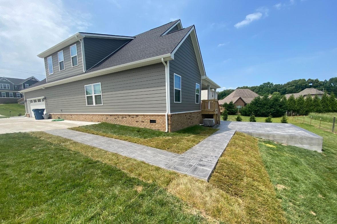 Suburban house with gray siding, brick foundation, and Stamped Concrete walkways on a sunny day