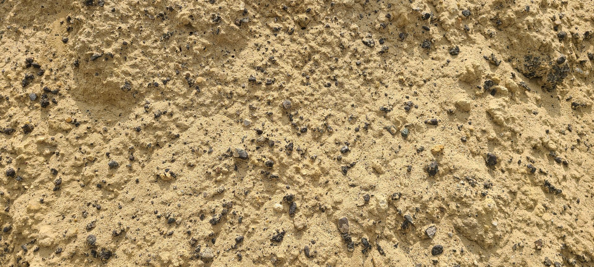 Close-up of beige sandy soil with scattered dark specks and small pebbles