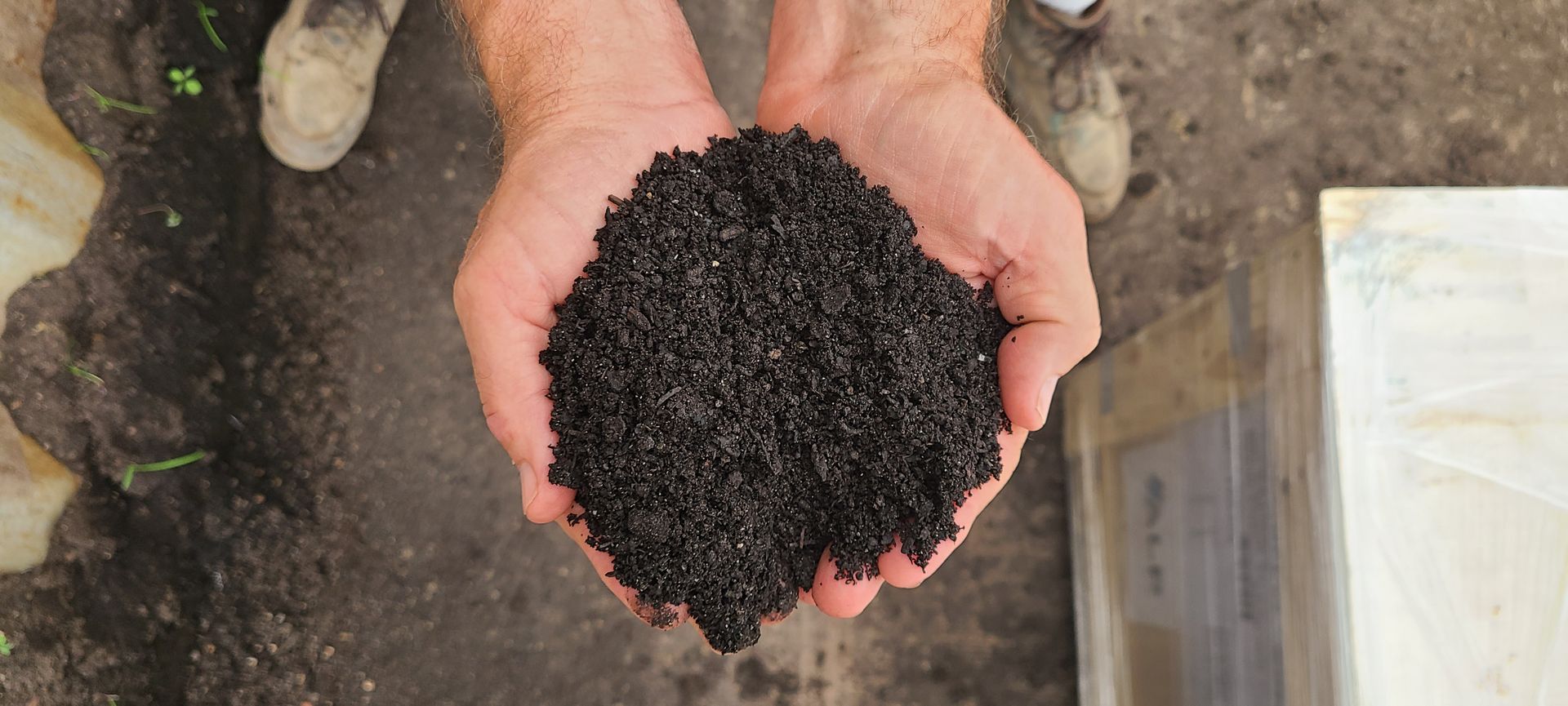 Hands holding a pile of dark pellets over soil outdoors