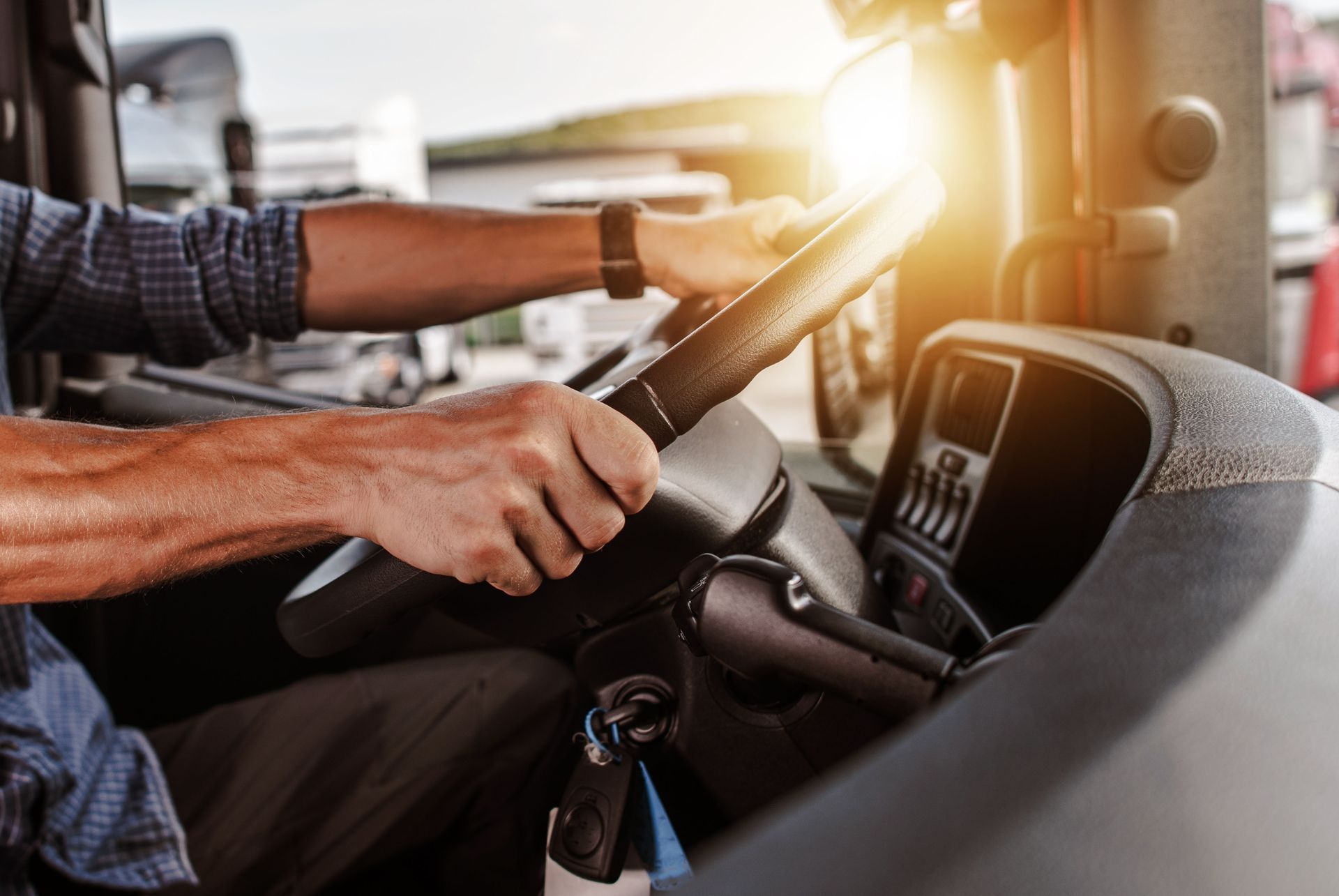 Hands gripping a steering wheel inside a truck cab, with bright sunlight streaming through the windshield.