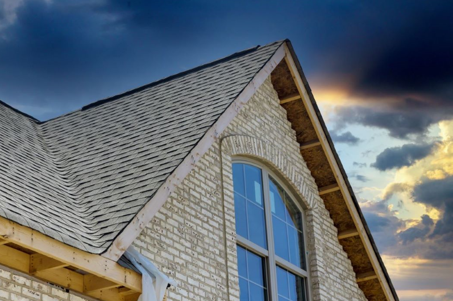 the roof of a brick house with a large window and a cloudy sky in the background