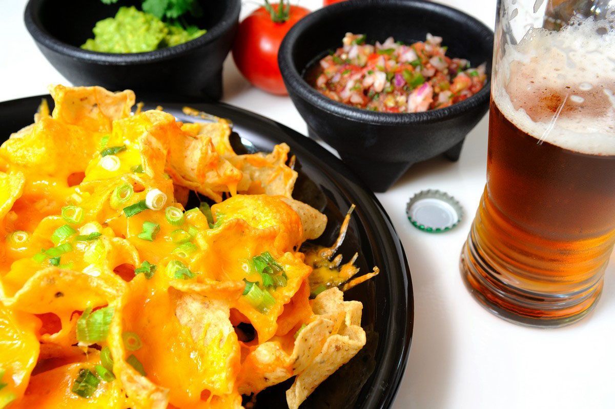 A bowl of nachos next to a glass of beer