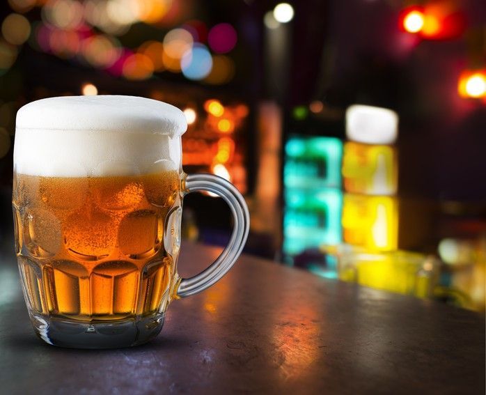 A glass of beer with foam on top is on a bar counter.